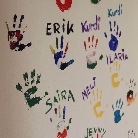 Zu sehen sind viele bunte Kinder-Händeabdrücke auf einer weißen Hand mit Unterschriften drunter.
